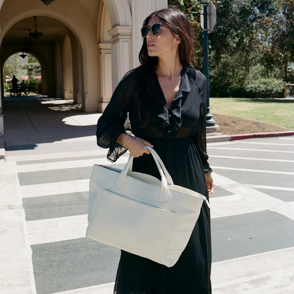 Woman in a black dress holding a white tote bag on a city street.