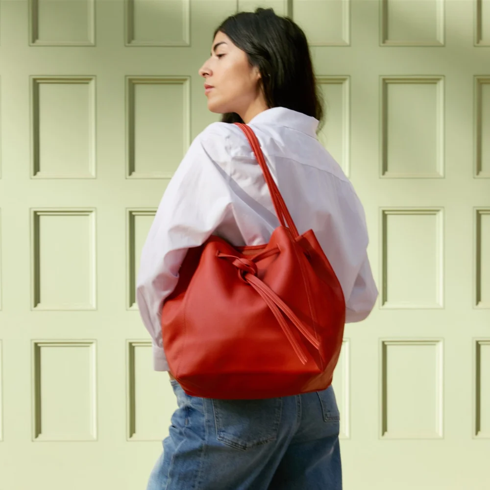 Woman carrying a red ORSYN tote bag against a light green wall