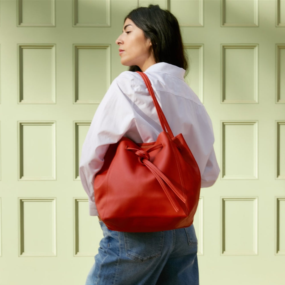 Woman carrying a red ORSYN tote bag against a light green wall