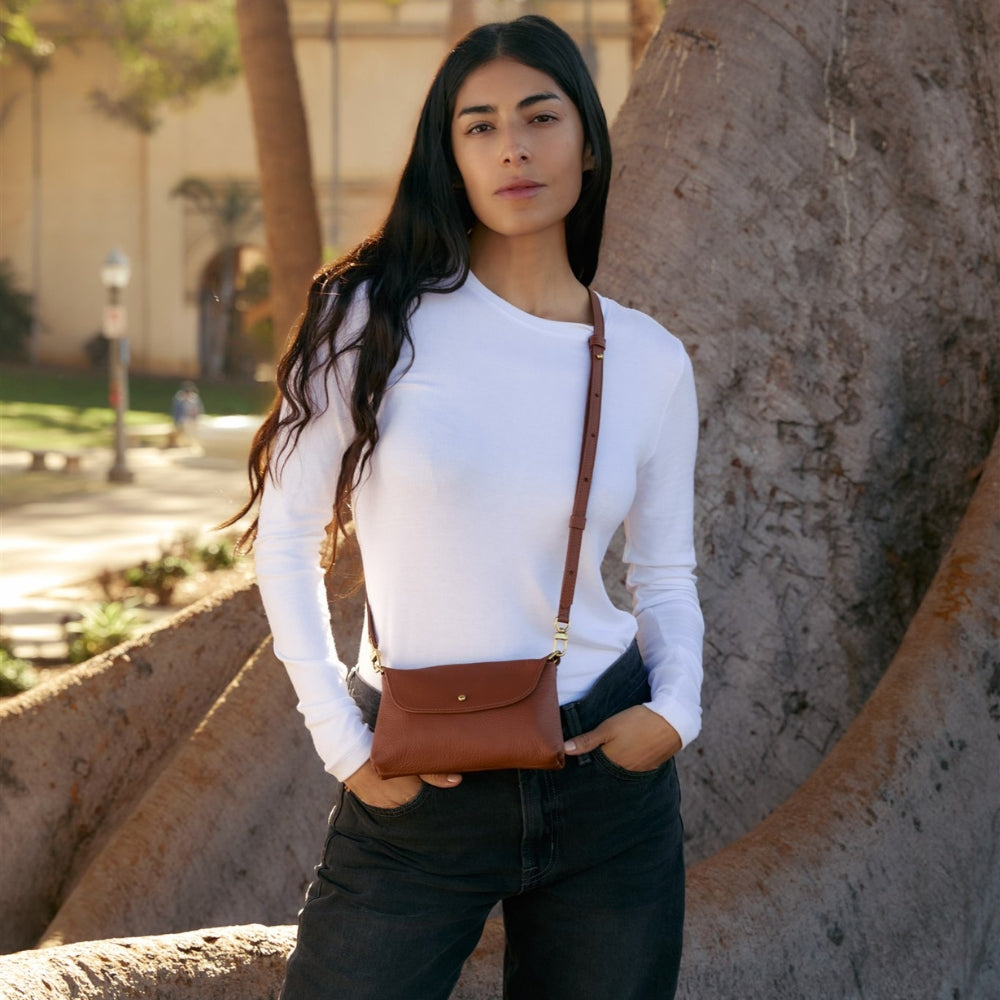 Woman wearing a brown leather crossbody bag in an outdoor setting