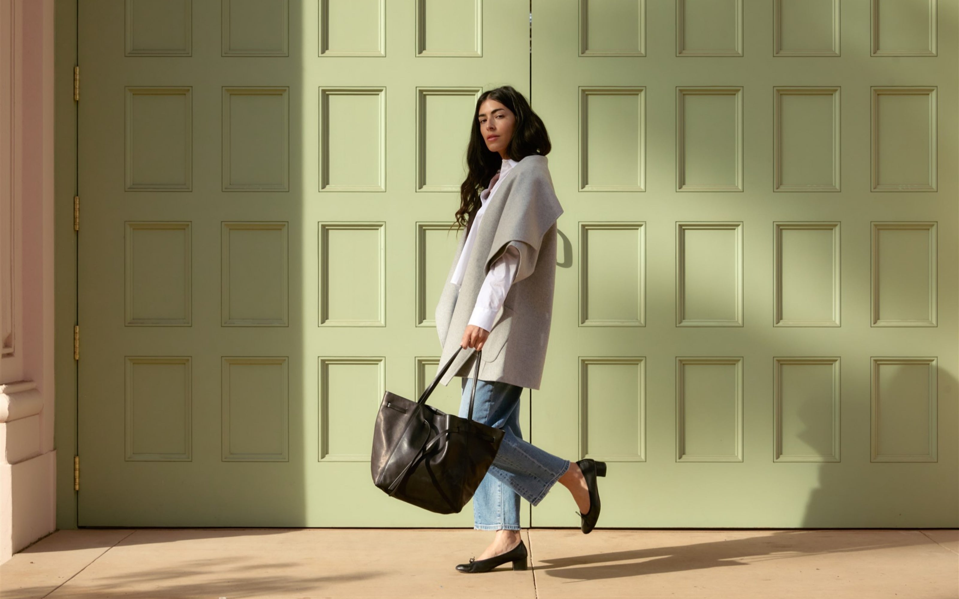 Woman holding a black ORSYN tote against a light green door