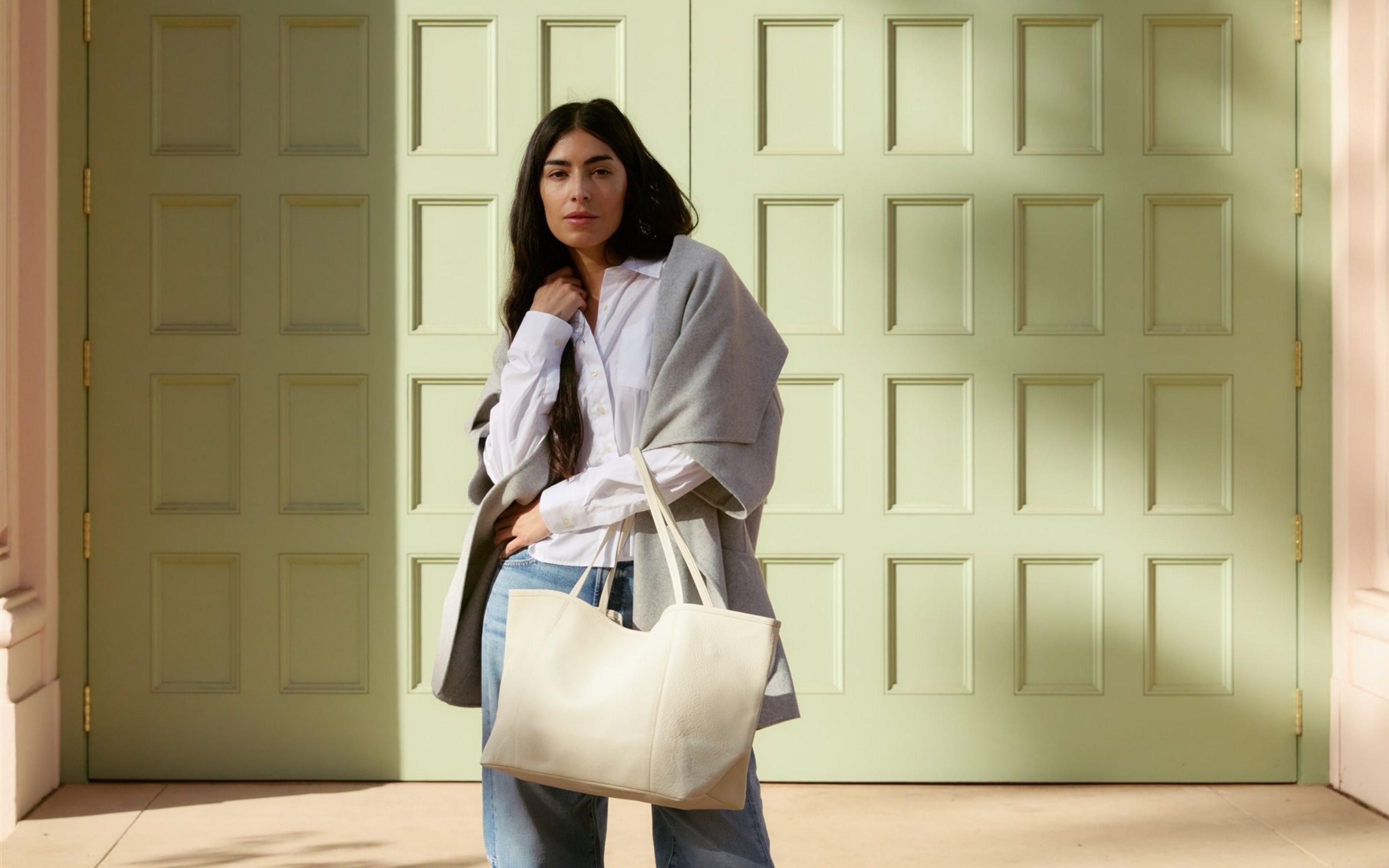 Woman holding a white ORSYN tote bag in front of a light green door.